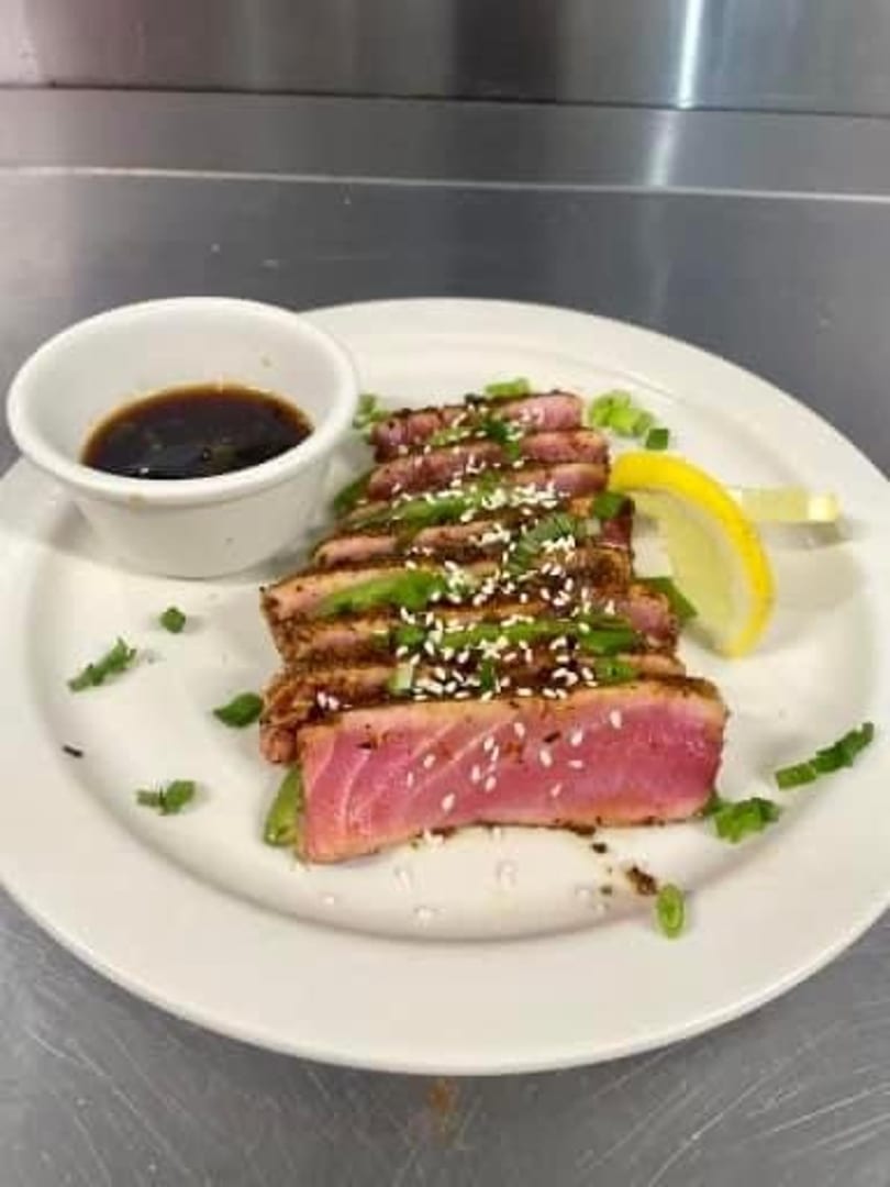 Seared tuna slices with sesame seeds, green onions, and a side of soy sauce and lemon.