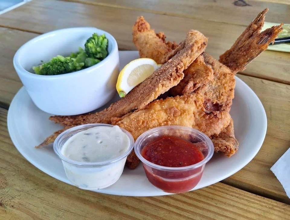 Fried fish with tails, a lemon wedge, broccoli, tartar sauce, and cocktail sauce on a white plate.
