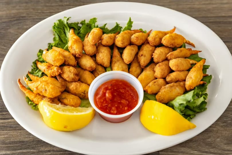 A white plate holds fried crab claws on lettuce, with cocktail sauce and lemon wedges.